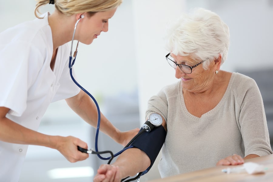 Frau vom Pflegedienst misst Blutdruck bei älterer Frau