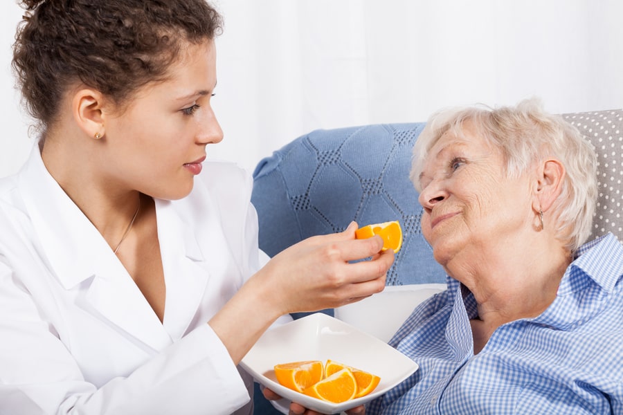 Frau vom Pflegedienst füttert bettlägerige ältere Frau mit Orangen