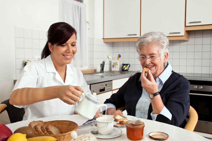 Altenpflegerin frühstückt mit Patientin im betreuten Wohnen